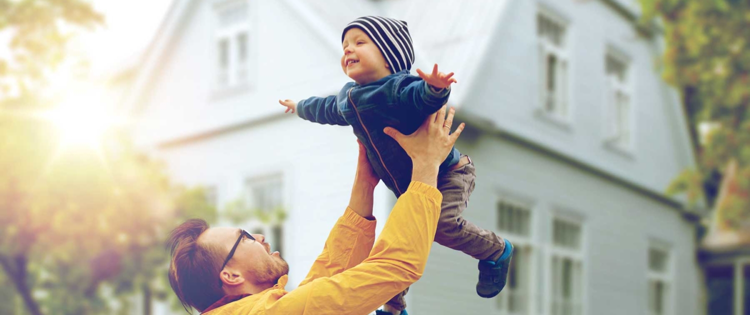 Family faither playfully tossing son in air in front of house